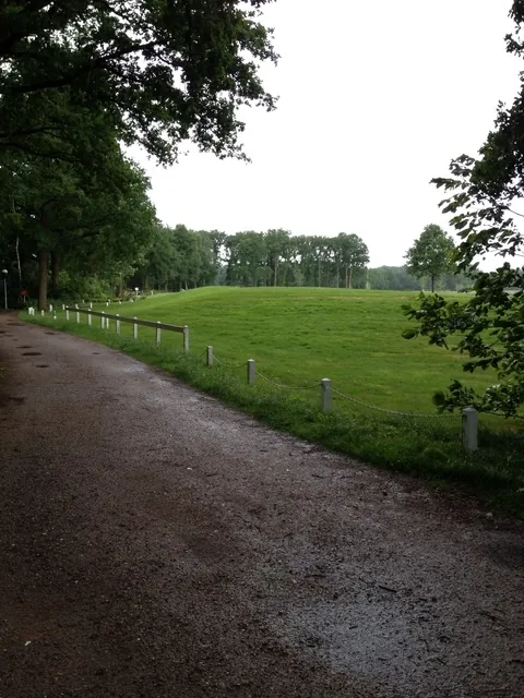 Een pad langs een groot grasveld met witte paaltjes.