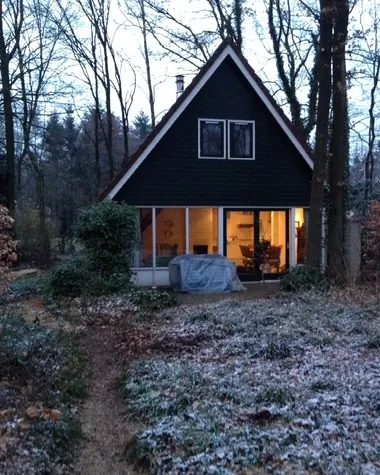 In de avond: de tuin is wit en achter de glazen pui brandt licht.