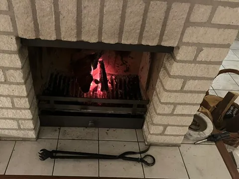 De open haard brandt, met de haardtang op de witte tegels ervoor.