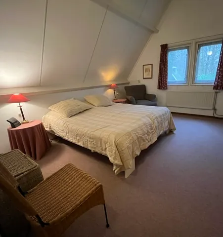 Dezelfde slaapkamer vanaf de andere kant, met een rieten stoel en een lamp met een rode kap.